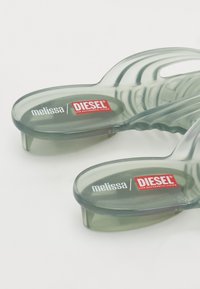 Gjennomsiktige grå sandaler med en teksturert overflate. Har 'melissa' og 'DIESEL' merking i hvitt og rødt. Unik rund design.