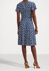 Marinblå blommig klänning med korta fladderärmar, figursydd midja och utsvängd kjol. Har vita mönster och en dragkedjedetalj bak.