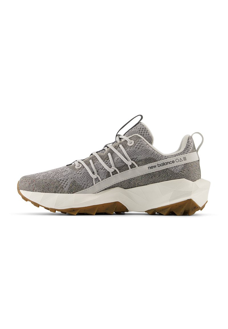 Grijze New Balance sneaker met een textuur van gebreid bovenwerk, witte geometrische zool, bruine profiel, elastisch vetersysteem en een trekband op de tong en hiel.