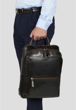 Mann iført blå skjorte og marineblå bukser, holder en mørk brun skinnmappe med to håndtak og glidelåslommer.