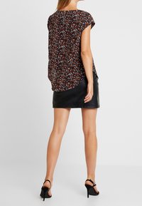 Blouse à imprimé floral en tissu sombre, avec des manches courtes et un col rond. Associée à une mini-jupe en cuir noir et des sandales à talons hauts.