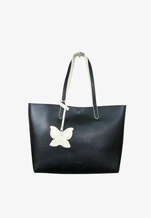Borsa tote in pelle nera con manici bianchi e un ciondolo bianco a forma di farfalla appeso a una tracolla.