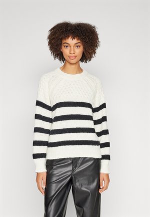 Weißer Pullover mit schwarzen horizontalen Streifen, strukturiertem Strickmuster und gerippten Bündchen und Saum. Kombiniert mit schwarzen Lederhosen.