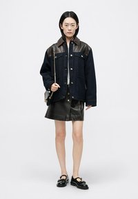 Dżinsowa kurtka z brązowymi skórzanymi ramionami, srebrnymi guzikami i dwiema przednimi kieszeniami. Połączona z czarną skórzaną spódnicą i ciemnymi butami.