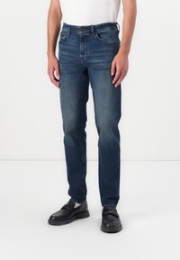 Donkerblauwe denim jeans met een rechte pijp, vijfzakkenontwerp en subtiele wassing. G gedragen met zwarte schoenen en een wit shirt.