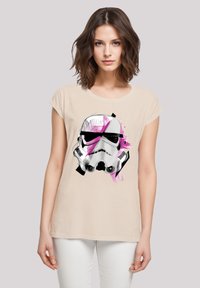Beiges kurzärmeliges T-Shirt mit Grafik eines Stormtrooper-Helms mit schwarzen und pinken abstrakten Akzenten. Weicher Stoff, lässiges Design.