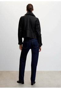 Czarna skórzana kurtka z sztucznym futrem przy kołnierzu, krótka konstrukcja, w połączeniu z ciemnoniebieskimi dżinsami. Gładka tekstura, minimalne detale.