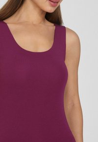 Fialový bezrukávový top s širokým kulatým výstřihem, vyrobený z měkké, elastické tkaniny. Hladká textura a přiléhavý design, vhodný pro vrstvení.