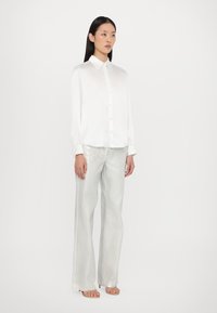 Witte blouse met lange mouwen, gecombineerd met glanzende zilveren brede broeken. De stof lijkt soepel met een lichte glans.