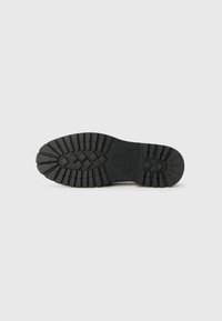 Black rubber boot sole with deep tread pattern, featuring a central logo and ridged edges for improved traction on various surfaces.