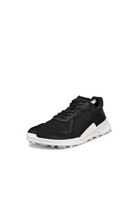 Czarne niskie trampki z białą teksturowaną podeszwą, z zapięciem na sznurowadła i wyściółką na kołnierzu, lekko pochylone w prawo na białym tle.