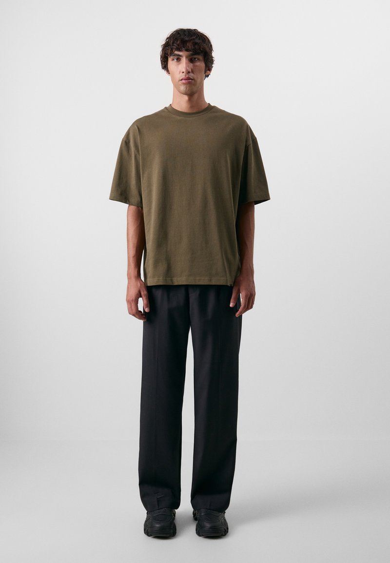 Olivengrøn oversized bomulds T-shirt med korte ærmer, parret med sorte vide bukser og mørke sneakers. Enkel, afslappet design.