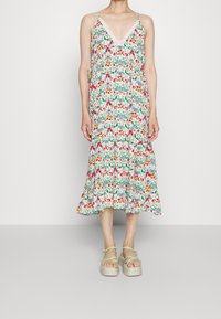 Abito midi floreale con una stampa bianca e colorata, dotato di spalline regolabili e bordi in pizzo, abbinato a sandali platform verde chiaro.