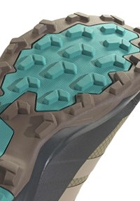 Close-up of a rugged shoe sole with teal and brown multi-directional rubber treads for enhanced grip and traction.