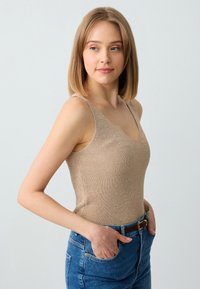 Beige geribbelde tanktop met een V-hals en dunne banden, gecombineerd met hoge blauwe spijkerbroek en een bruine riem, met een aansluitend ontwerp.