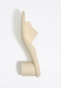Beige instapper met een ronde blokhak en een gebogen bovenkant, vanaf de zijkant weergegeven op een witte achtergrond.