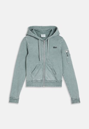 Haut à capuche zippé bleu clair avec une poche avant, un capuchon avec cordon de serrage, petit logo sur la poitrine et poche zippée sur la manche gauche.