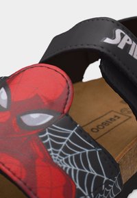Παιδικό σανδάλι που διαθέτει κόκκινο γραφικό πρόσωπο Spider-Man, μαύρο λουράκι με μερική επιγραφή "Spider" και πάτο από φελλό με την ένδειξη "Bamboo".