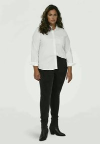 Bijela košulja s dugim rukavima, uparena s crnim uskim hlačama. Glatka tkanina s klasičnim dizajnom, uskog kroja i gležnjačama.