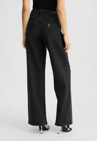 Jeans neri a gamba larga con vita alta, caratterizzati da una trama in denim liscia, due tasche posteriori e dettagli in strass lungo le cuciture laterali.