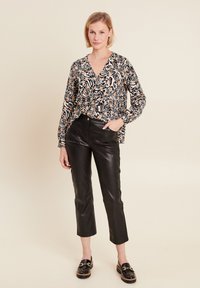 Langarmblouse met V-hals in een zwart en oranje bloemenpatroon, gecombineerd met hoog uitgesneden zwarte neplederen cropped pants en zwarte instappers.