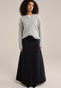 Svetlo siva pletena cardigan s gumbi, v kombinaciji z dolgo črno jeans krilo, ki prikazuje gladko teksturo in ravno silhueto.