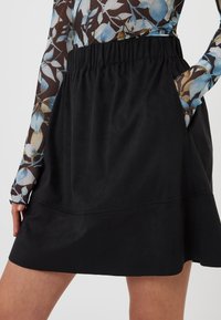 Jupe noire avec une taille élastique, présentant une texture lisse et une forme évasée. Les poches latérales ajoutent une fonctionnalité au design.