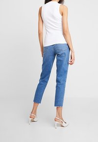 Top sin mangas de rayas blancas combinado con jeans de tiro alto azules, con un dobladillo sin terminar. El conjunto se completa con sandalias de tacón blancas.