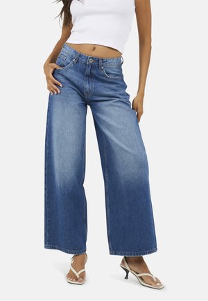 Brede spijkerbroek van blauw denim met een hoge taille, vervaagde afwerking en een vijf-pocket ontwerp. Gecombineerd met lichtgekleurde sandalen met hakken.