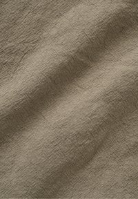 Tissu beige texturé avec des plis visibles et un motif de tissage légèrement grossier, montrant des plis doux et des ombres.
