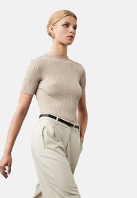 Beige geribbelde trui met korte mouwen, ronde halslijn en een textuurfinish, gecombineerd met lichtbeige broek en een zwarte riem.