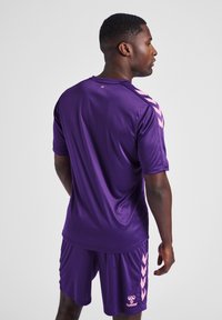 Purple athletic jersey and shorts with pink accents, featuring a smooth texture and chevron design on the sleeves. Brand logo visible.