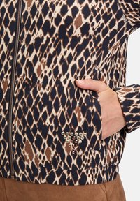 Veste marron et marine à motifs avec fermeture éclair, présentant un imprimé animal texturé et un accent en bijoux sur la poche.