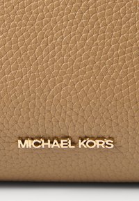 Portefeuille en cuir texturé couleur noisette avec un logo "MICHAEL KORS" en ton doré. Présente une finition grainée et un design minimaliste.