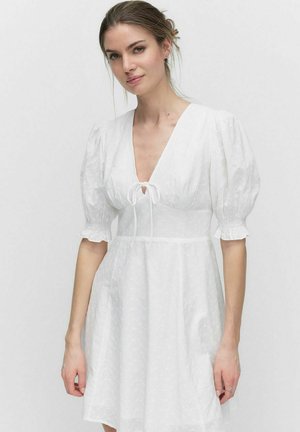 Robe blanche à manches bouffantes courtes, décolleté en V profond et détail à cordon au niveau du col. Tissu léger et texturé avec un motif subtil.