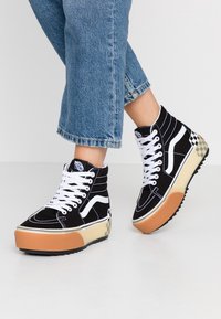 Černé plátěné vysoké tenisky s bílými akcenty, s platformovou podrážkou a kostkovaným vzorem na patě. Bílé tkaničky a prošívání.