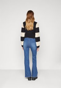 Schwarz-weißer gestreifter Strickpullover mit langen Ärmeln, kombiniert mit blauen Schlagjeans und schwarzen Plateau-Stiefeln. Rückansicht.