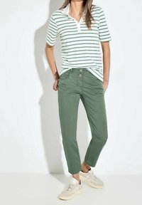 Gestreepte polo met korte mouwen in wit en groen, gecombineerd met olijfgroene tapered broek en lichtgekleurde sneakers. Slim fit design, casual uitstraling.