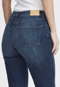 Tmavomodré džínsy s úzkym strihom, s koženou nášivkou s nápisom "PULZ JEANS," piatimi vreckami a jemnými detailmi na šití.