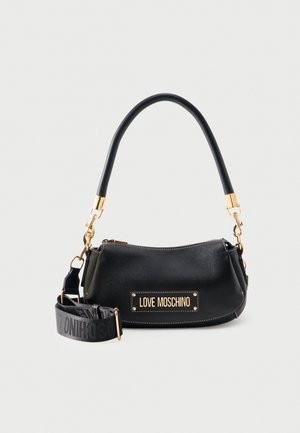 Čierna kabelka Moschino so zlatým kovaním, odnímateľným popruhom cez rameno s logom a zakrivenou rukoväťou na jednoduchom svetlom pozadí.