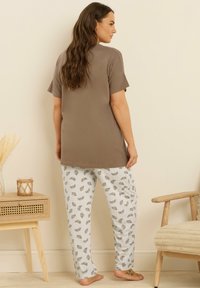 Ljust brunt kortärmat plagg i kombination med vita pyjamasbyxor med ett grått croissantmönster. Mjuk tygkvalitet och avslappnad passform lyfts fram.