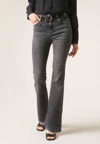 Jean noir évasé en denim à la texture lisse. Doté d'une taille mi-haute et de poches avant. Associé à de simples sandales à talons noirs.
