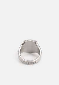Silverring med polerat yta, med en graverad "GUESS"-logotyp på bandet och en dekorativ design upptill.