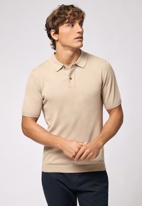 Polo shirt beige a maniche corte con colletto e chiusura a due bottoni. Tessuto liscio, forma aderente e piccolo logo dettagliato all'orlo.