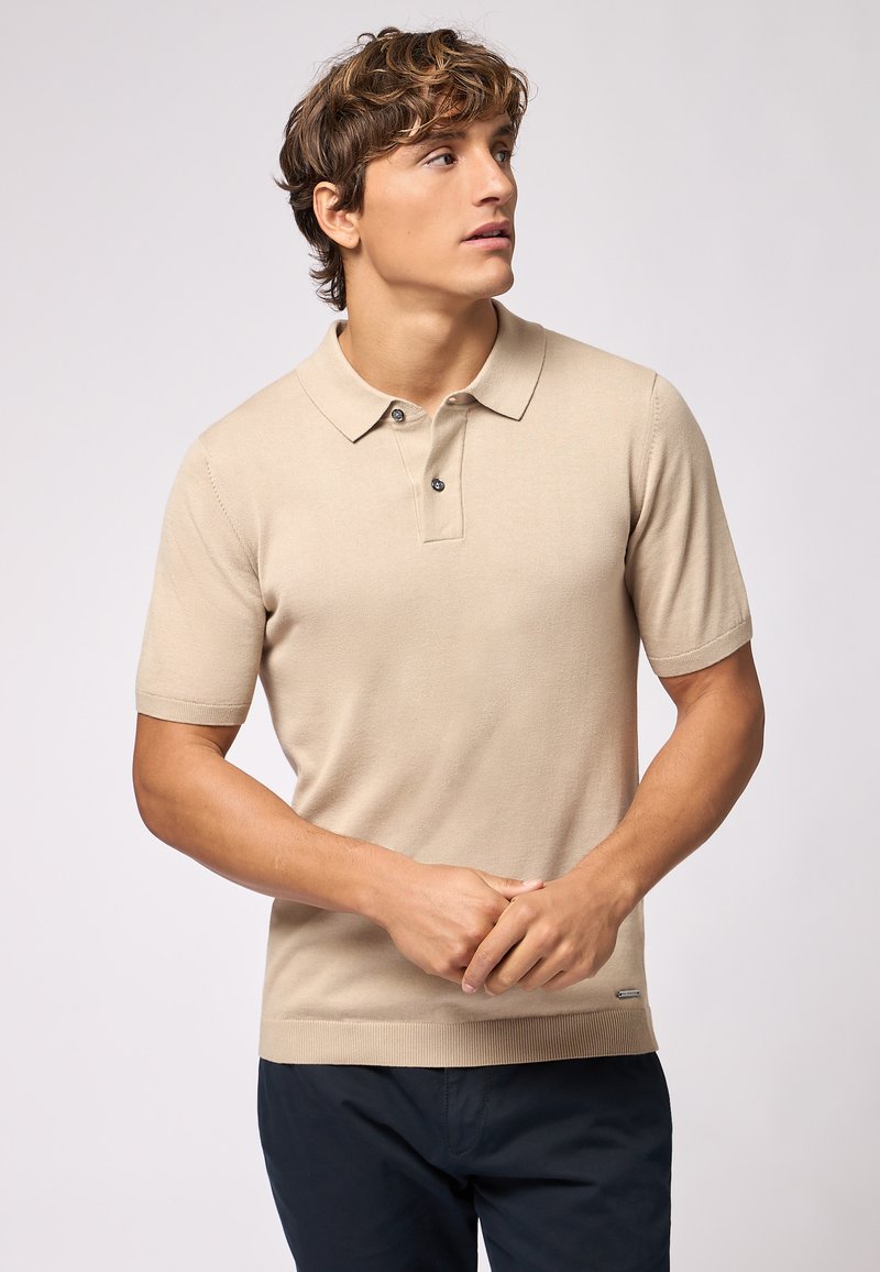 Polo shirt beige a maniche corte con colletto e chiusura a due bottoni. Tessuto liscio, forma aderente e piccolo logo dettagliato all'orlo.
