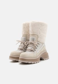 Beige snørestøvler til vinter med tykke rillede såler, faux pelskanter og shimmer mesh stofdetaljer på hvid baggrund.