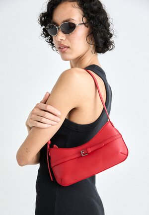 Rote Ledertasche mit glatter Textur, geschwungenem Design und dekorativem Schnallenakzent. Verstellbarer Schulterriemen und Reißverschlussverschluss.