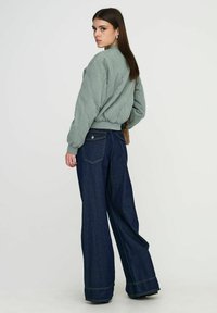 Blouson aviateur matelassé vert clair avec poignets et ourlet côtelés, associé à un jean en denim foncé à coupe ample, avec poches arrière et jambes larges.