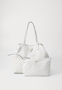 Sac fourre-tout blanc et porte-poignet assorti avec motif géométrique et logos Guess en métal doré sur un fond uni.