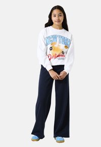 White sweatshirt with "NEW YORK" graphic in blue and red, paired with navy striped wide-leg pants and light blue sneakers.